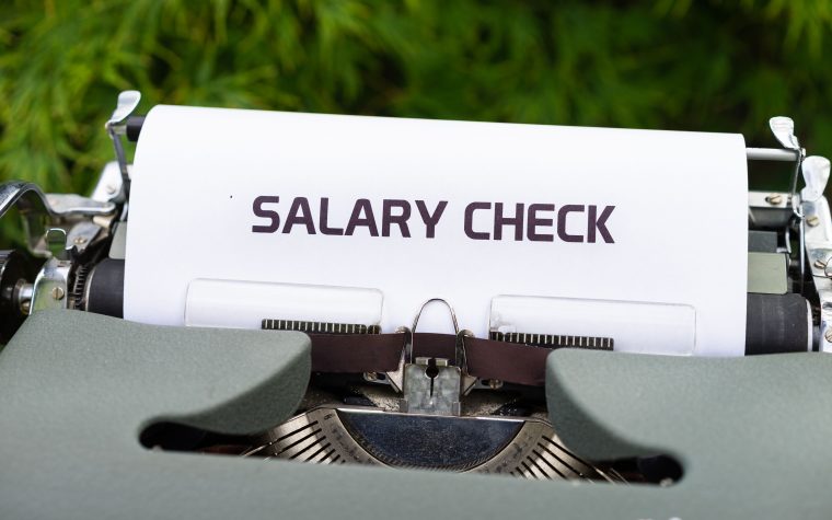 Close-up of a vintage typewriter typing 'Salary Check' on paper, symbolizing payroll and finance. Gros plan d'une machine à écrire vintage tapant "Salary Check" sur du papier, symbolisant la paie et les finances.