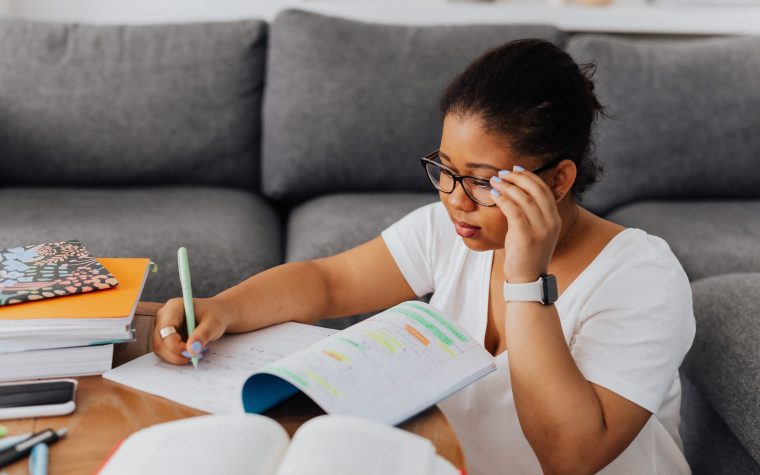 A young woman wearing glasses studies with a notebook on a table indoors, highlighting focus and learning. Une jeune femme portant des lunettes étudie avec un carnet sur une table à l'intérieur, mettant l'accent sur la concentration et l'apprentissage.