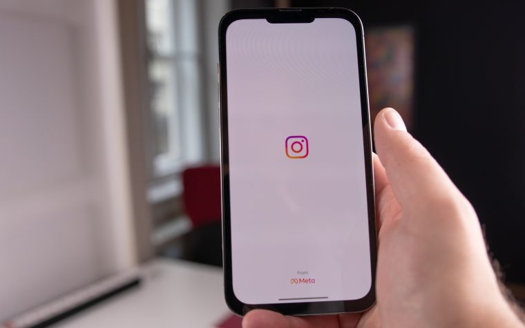 Close-up of a hand holding a smartphone displaying the Instagram app, indoors in Budapest. Gros plan d'une main tenant un smartphone affichant l'application Instagram, en intérieur à Budapest.