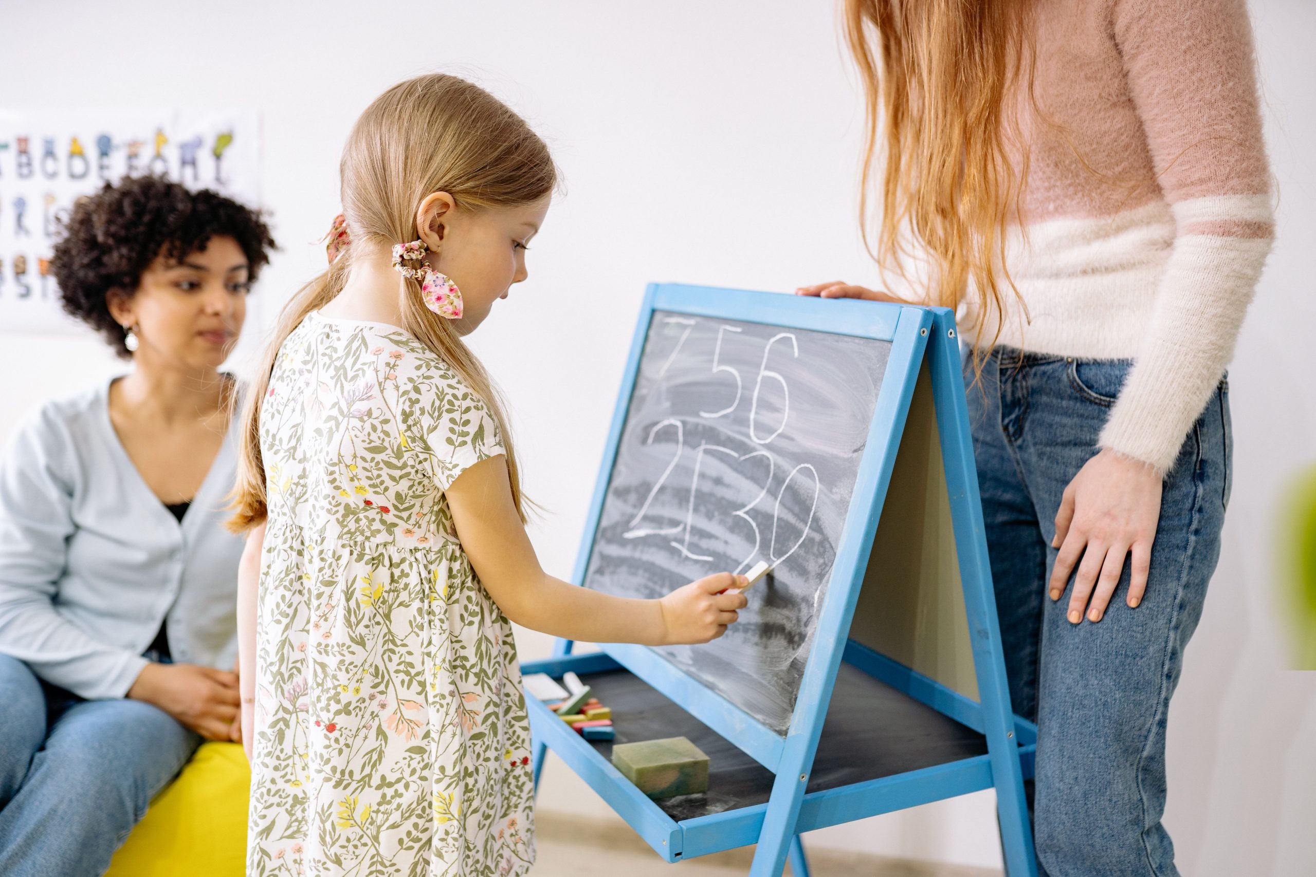 Fillette écrivant des chiffres au tableau sous supervision