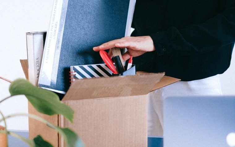 Adult woman organizing office supplies into a cardboard box, possibly symbolizing job change or relocation. Une femme adulte organisant des fournitures de bureau dans une boîte en carton, symbolisant peut-être un changement d'emploi ou une relocalisation.